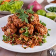 Spicy minced chicken on a white plate complete with cucumber, lettuce and side dishes on wooden table.